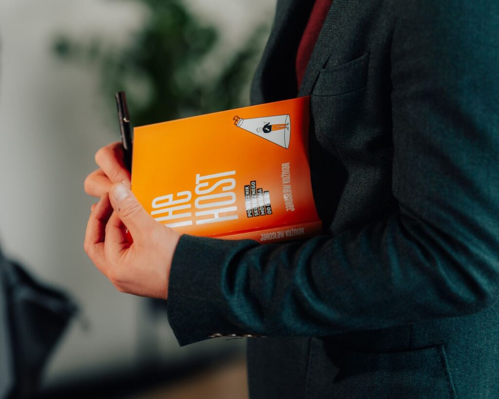 Mężczyzna trzyma podręcznik The Host Jarosława Kuźniara – książkę o sztuce wystąpień publicznych